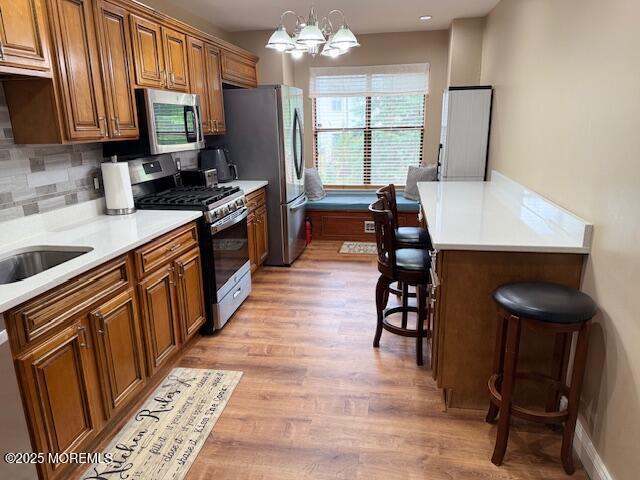 372 Oak Knoll Dr, Manalapan, NJ 07726 - kitchen featuring appliances with stainless steel finishes, brown cabinetry, a kitchen breakfast bar, and light wood-style flooring