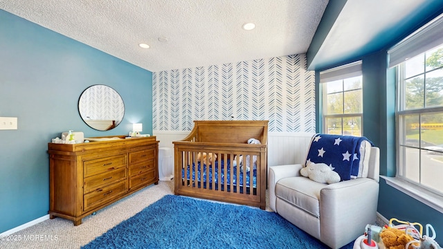 280 Tulip Ln, Freehold, NJ 07728 - carpeted bedroom featuring wallpapered walls, a textured ceiling, an accent wall, a wainscoted wall, and a nursery area