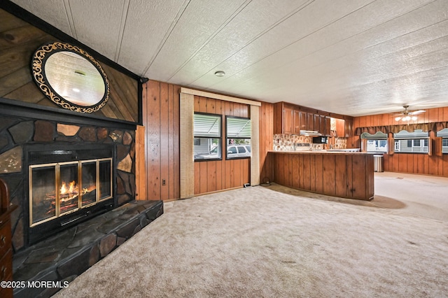 119 Village Rd, Morganville, NJ 07751 - kitchen featuring wooden walls, carpet flooring, a stone fireplace, open floor plan, and brown cabinets