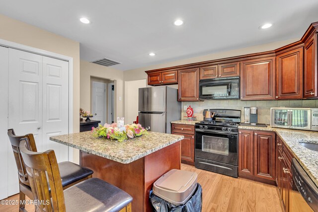 87 Prince Charles Dr, Toms River, NJ 08757 - kitchen with black appliances, light wood-style floors, a kitchen breakfast bar, decorative backsplash, and light stone countertops