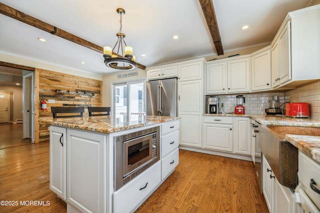 13 Poplar Ave, Fair Haven, NJ 07704 - kitchen featuring appliances with stainless steel finishes, beamed ceiling, white cabinetry, decorative backsplash, and a center island