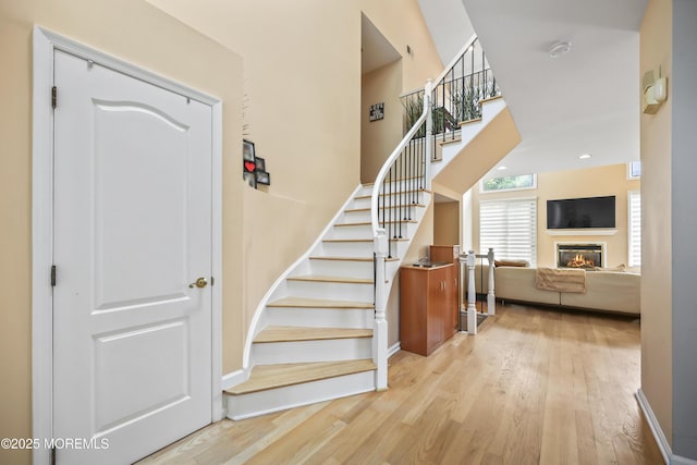 117 Sequoia Woods Ct, Holmdel, NJ 07733 - staircase featuring wood finished floors, a glass covered fireplace, baseboards, and a towering ceiling