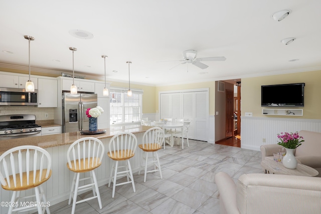 3 Watson Pl, Manasquan, NJ 08736 - kitchen featuring appliances with stainless steel finishes, a ceiling fan, a kitchen bar, crown molding, and wainscoting