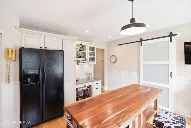 15 Tanglewood Dr, Barnegat, NJ 08005 - kitchen featuring black refrigerator with ice dispenser, a barn door, a wainscoted wall, a textured ceiling, and glass insert cabinets