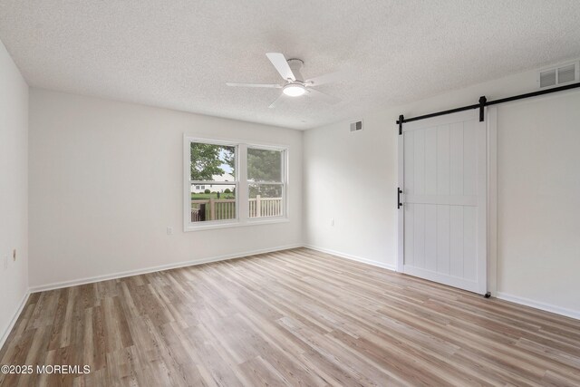 21 Turnbridge, Manchester, NJ 08759 - unfurnished room with light wood-style floors, a barn door, a ceiling fan, a textured ceiling, and baseboards