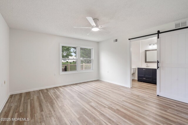 21 Turnbridge, Manchester, NJ 08759 - unfurnished bedroom featuring a barn door, light wood-type flooring, a textured ceiling, connected bathroom, and baseboards
