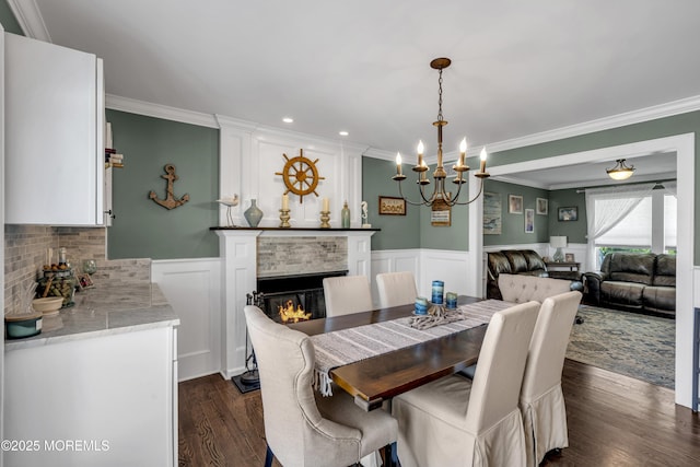 913 Lorillard Ave, Union Beach, NJ 07735 - dining area with crown molding, dark wood finished floors, a chandelier, a lit fireplace, and wainscoting