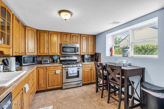 1208 Pine Tree Way, Belmar, NJ 07719 - kitchen featuring stainless steel appliances, a sink, brown cabinets, tasteful backsplash, and glass insert cabinets