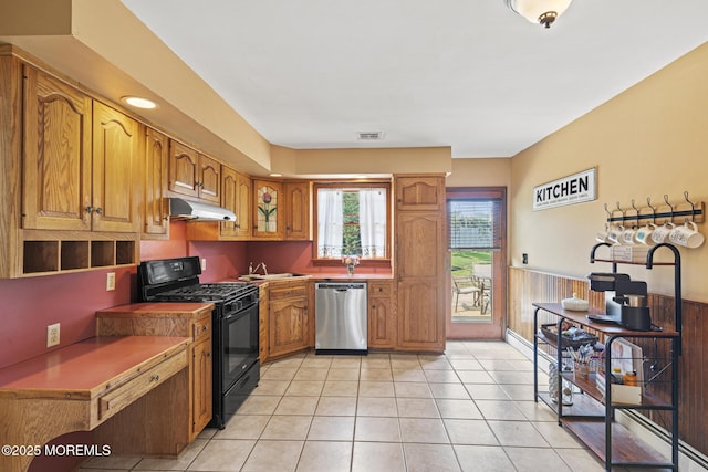 1172 Laurel Dr, Toms River, NJ 08753 - kitchen featuring dishwasher, black gas range oven, under cabinet range hood, brown cabinetry, and a wainscoted wall