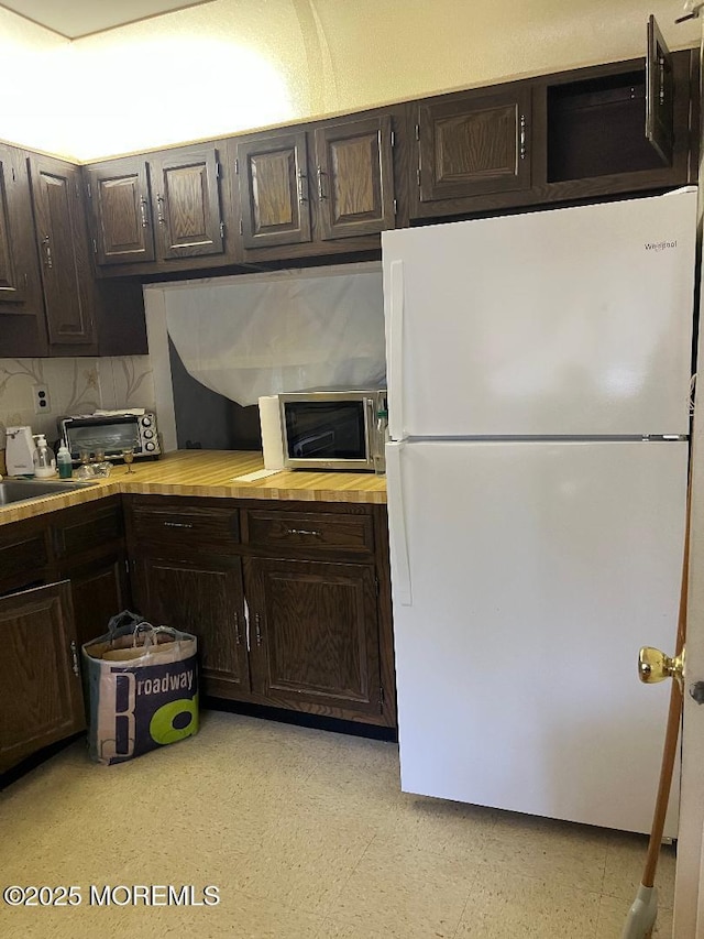 212 Covered Bridge Blvd Unit D, Manalapan, NJ 07726 - kitchen with freestanding refrigerator, stainless steel microwave, dark brown cabinetry, light floors, and wood counters