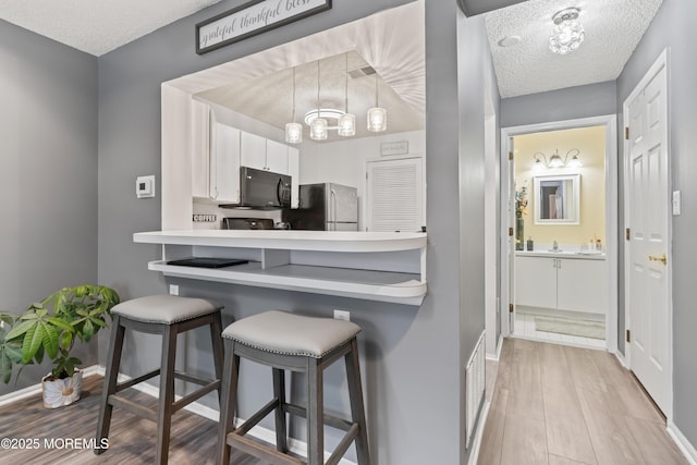 70 Madison Ct, Tinton Falls, NJ 07712 - kitchen featuring black microwave, freestanding refrigerator, a textured ceiling, wood finished floors, and a breakfast bar area