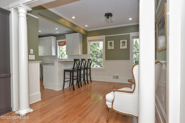 51 Clay St, Fair Haven, NJ 07704 - kitchen with decorative columns, a kitchen bar, a wainscoted wall, light wood finished floors, and ornamental molding