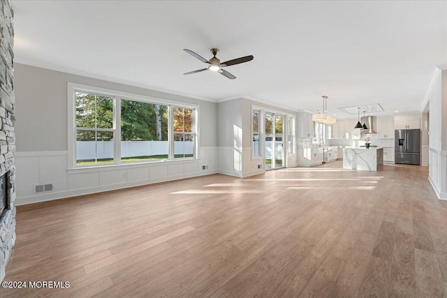 1119 Northstream Pkwy, Point Pleasant, NJ 08742 - unfurnished living room featuring crown molding, a stone fireplace, a ceiling fan, light wood-style floors, and a wainscoted wall
