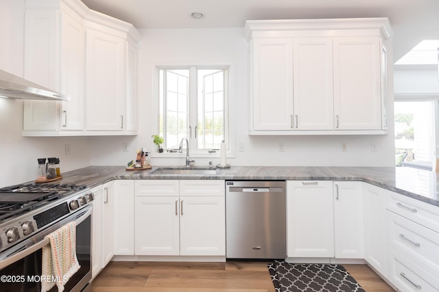 10 English Path, Freehold, NJ 07728 - kitchen featuring appliances with stainless steel finishes, wall chimney range hood, white cabinetry, light stone counters, and light wood-style floors