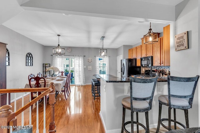 9 Olivia Dr, Tinton Falls, NJ 07712 - kitchen featuring black microwave, refrigerator with ice dispenser, a kitchen breakfast bar, light wood finished floors, and decorative backsplash