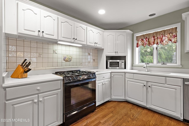 14 W St, Monmouth Beach, NJ 07750 - kitchen featuring appliances with stainless steel finishes, white cabinetry, decorative backsplash, light wood-style floors, and light countertops