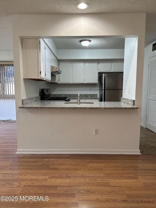 115 Brandywine Ct Unit 115, Brick, NJ 08724 - kitchen with freestanding refrigerator, wall chimney exhaust hood, a peninsula, gas range oven, and wood finished floors