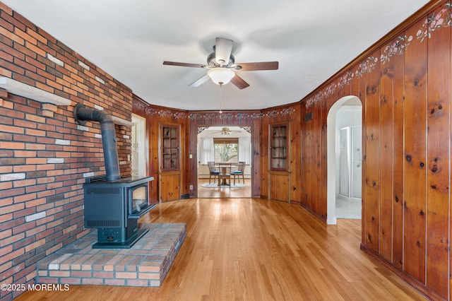 149 9th St, Belford, NJ 07718 - unfurnished living room with arched walkways, a wood stove, brick wall, a ceiling fan, and light wood-style flooring