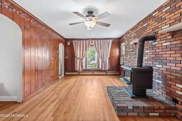 149 9th St, Belford, NJ 07718 - unfurnished living room with arched walkways, light wood-style floors, a ceiling fan, a wood stove, and brick wall