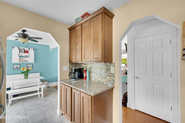 5 Robert Ave, Howell, NJ 07731 - kitchen featuring backsplash, light stone counters, ceiling fan, brown cabinets, and light tile patterned flooring