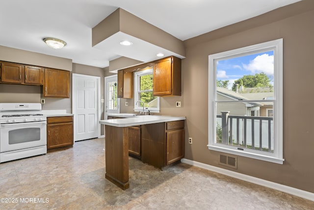 76 9th St, Belford, NJ 07718 - kitchen featuring white range with gas stovetop, light countertops, a peninsula, and brown cabinetry