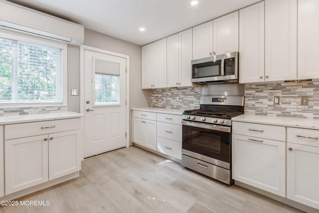 6 S Heron St Unit A, Manchester, NJ 08759 - kitchen featuring appliances with stainless steel finishes, a wall unit AC, backsplash, light wood-style floors, and white cabinets