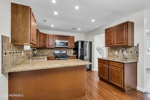 1217 Madison Ave, Toms River, NJ 08757 - kitchen featuring appliances with stainless steel finishes, a peninsula, dark wood-type flooring, backsplash, and light stone counters