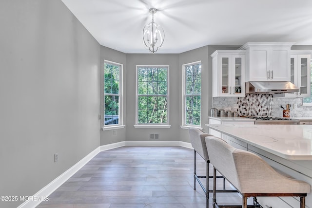 8 Armistead Ky, Colts Neck, NJ 07722 - kitchen with under cabinet range hood, white cabinets, light stone counters, tasteful backsplash, and light wood finished floors