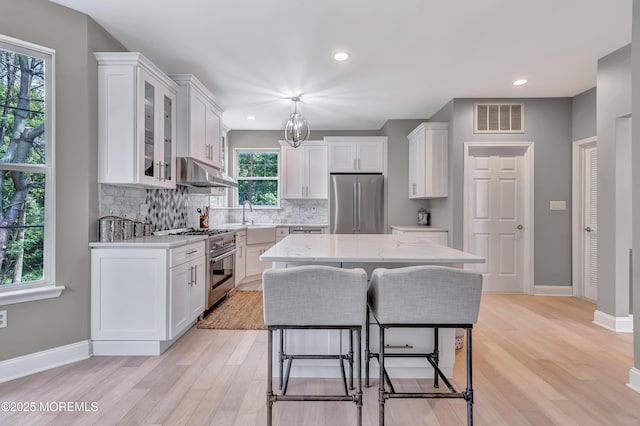 8 Armistead Ky, Colts Neck, NJ 07722 - kitchen with stainless steel appliances, under cabinet range hood, light wood finished floors, white cabinetry, and decorative backsplash