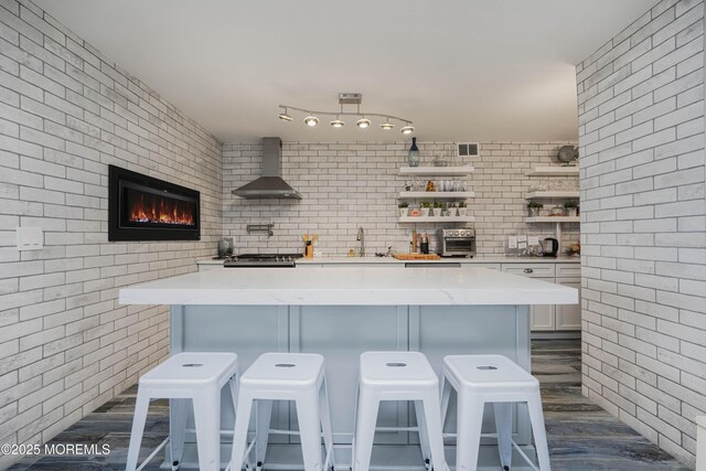 675 Ocean Ave Unit 5J, Long Branch, NJ 07740 - kitchen featuring wall chimney range hood, open shelves, white cabinets, a kitchen breakfast bar, and a glass covered fireplace