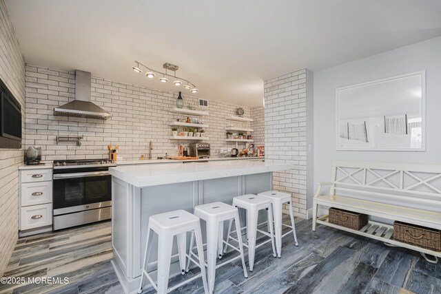 675 Ocean Ave Unit 5J, Long Branch, NJ 07740 - kitchen featuring stainless steel range oven, wall chimney range hood, a kitchen bar, wood finished floors, and brick wall