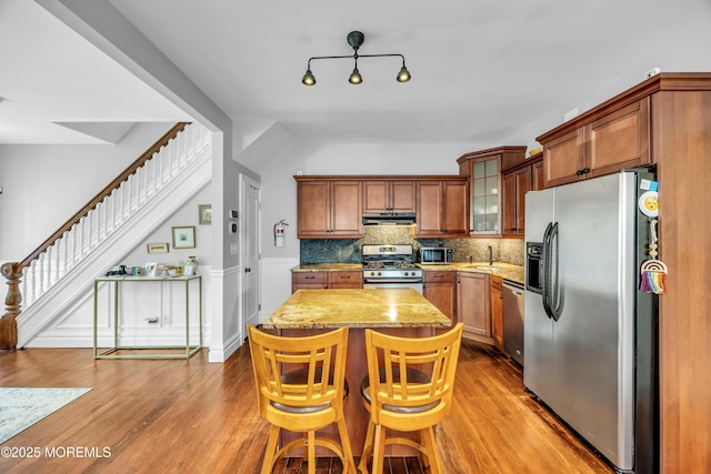 1108 Emory St, Asbury Park, NJ 07712 - kitchen with appliances with stainless steel finishes, under cabinet range hood, a center island, light stone countertops, and brown cabinetry