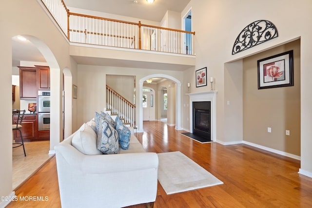 19 E Francesa Ct, Farmingdale, NJ 07727 - living area featuring a high ceiling, arched walkways, light wood-type flooring, a glass covered fireplace, and stairs
