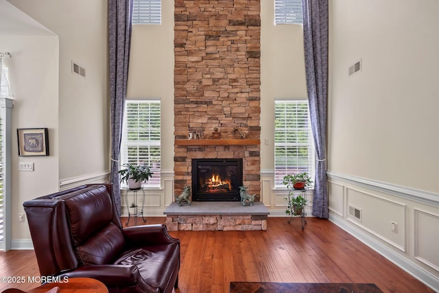 86 Legacy Ct, Freehold, NJ 07728 - living room featuring a towering ceiling, healthy amount of natural light, a stone fireplace, hardwood / wood-style floors, and wainscoting