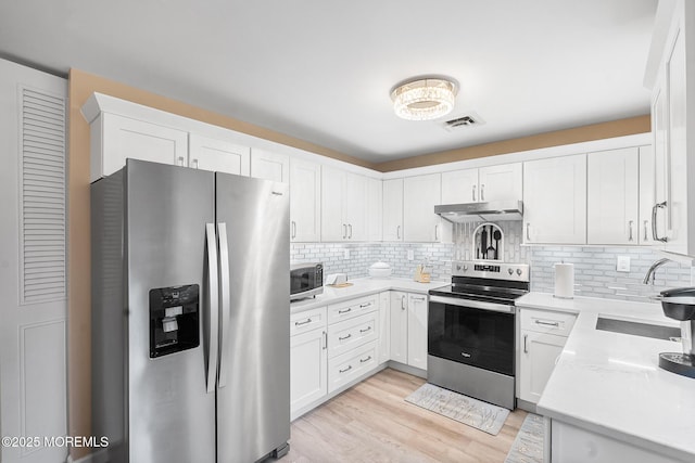1058A Argyll Cir, Lakewood, NJ 08701 - kitchen featuring stainless steel appliances, under cabinet range hood, decorative backsplash, light wood-style flooring, and light countertops