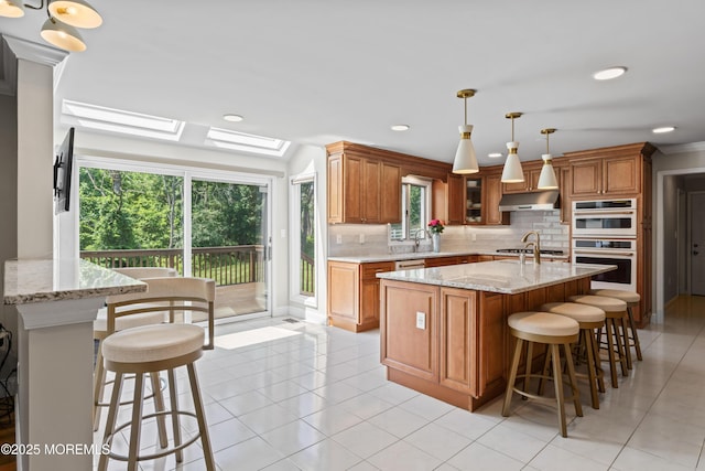 20 Birch Ln, Colts Neck, NJ 07722 - kitchen with a skylight, brown cabinetry, decorative backsplash, under cabinet range hood, and appliances with stainless steel finishes