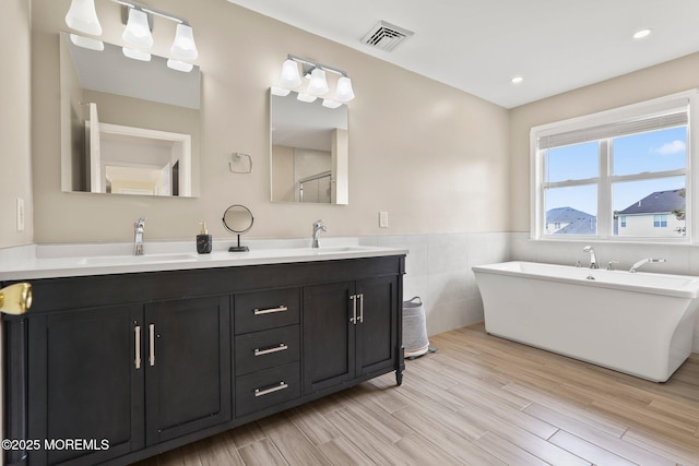 43 Shawnee Way, Morganville, NJ 07751 - bathroom with double vanity, a freestanding tub, wood finished floors, tile walls, and a wainscoted wall