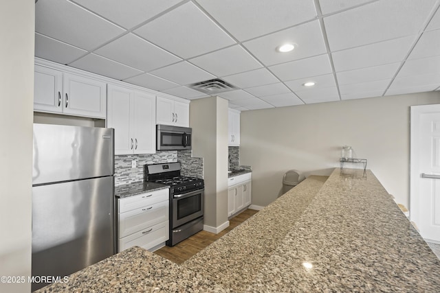 675 Ocean Ave # 9F, Long Branch, NJ 07740 - kitchen featuring stainless steel appliances, dark wood-style flooring, a paneled ceiling, white cabinets, and tasteful backsplash