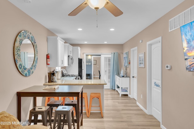 241 Hiering Ave, Seaside Heights, NJ 08751 - kitchen with stainless steel microwave, light wood-style floors, white cabinetry, a ceiling fan, and a peninsula