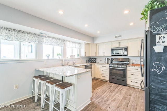 887 Beach Haven W Blvd, Manahawkin, NJ 08050 - kitchen with stainless steel appliances, a peninsula, light stone countertops, light wood-style floors, and a kitchen bar