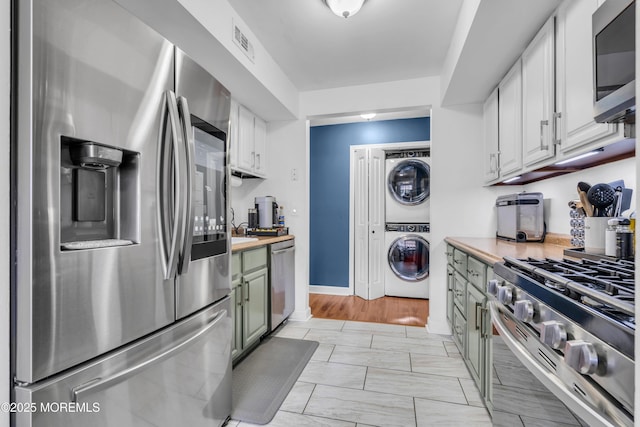 193 Sierra Ct, Woodbridge, NJ 07095 - kitchen with appliances with stainless steel finishes, estacked washer and dryer, light countertops, light marble finish flooring, and white cabinetry