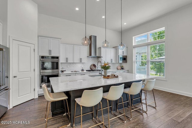 2 Foulks Ter, Lincroft, NJ 07738 - kitchen with wall chimney range hood, stainless steel appliances, a towering ceiling, a kitchen island with sink, and white cabinets