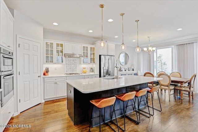 2 Lawley Dr, Lincroft, NJ 07738 - kitchen with appliances with stainless steel finishes, a breakfast bar, light wood-style floors, glass insert cabinets, and a center island with sink