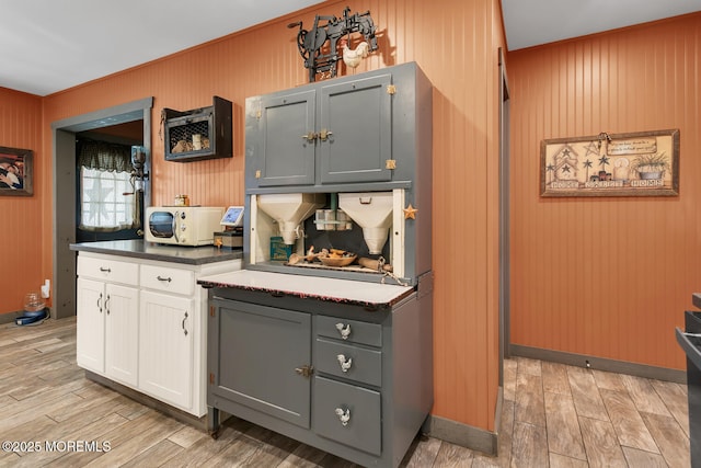 216 Main St, Port Monmouth, NJ 07758 - kitchen with white cabinetry, wood walls, stainless steel microwave, dark countertops, and light wood-style flooring