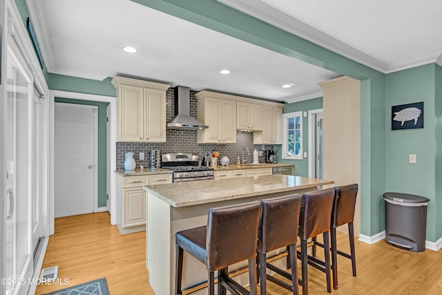 384 Gerry Rd, North Brunswick, NJ 08902 - kitchen featuring appliances with stainless steel finishes, wall chimney range hood, cream cabinetry, light wood-style flooring, and ornamental molding