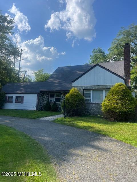 411 Brookside Ave, Oakhurst, NJ 07755 - ranch-style home featuring a chimney, a front yard, stone siding, board and batten siding, and driveway