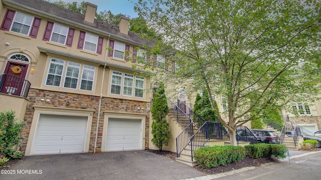 56 W Aspen Way, Aberdeen, NJ 07747 - townhome / multi-family property with stone siding, asphalt driveway, stairs, a chimney, and an attached garage