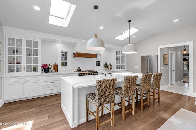 6 Buttonwood Dr, Shrewsbury Boro, NJ 07702 - kitchen with a skylight, vaulted ceiling, light wood-style floors, glass insert cabinets, and an island with sink