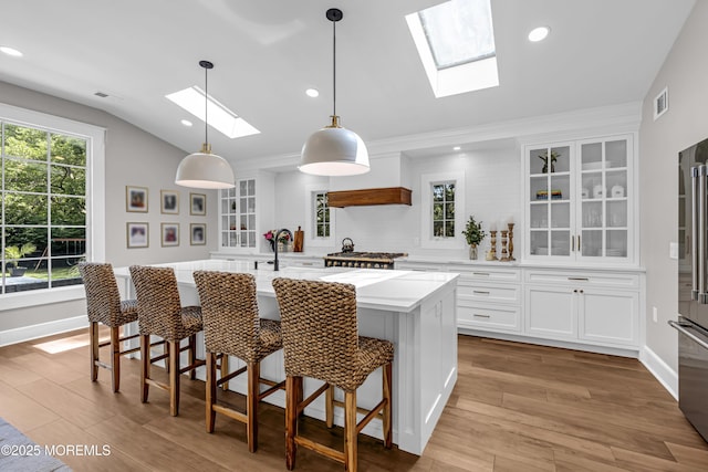 6 Buttonwood Dr, Shrewsbury Boro, NJ 07702 - kitchen featuring a skylight, a center island with sink, white cabinetry, glass insert cabinets, and light wood-style floors