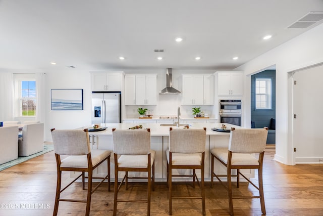 37 Longwood Dr, Monroe, NJ 08831 - kitchen featuring stainless steel appliances, wall chimney exhaust hood, a kitchen island with sink, light countertops, and a breakfast bar